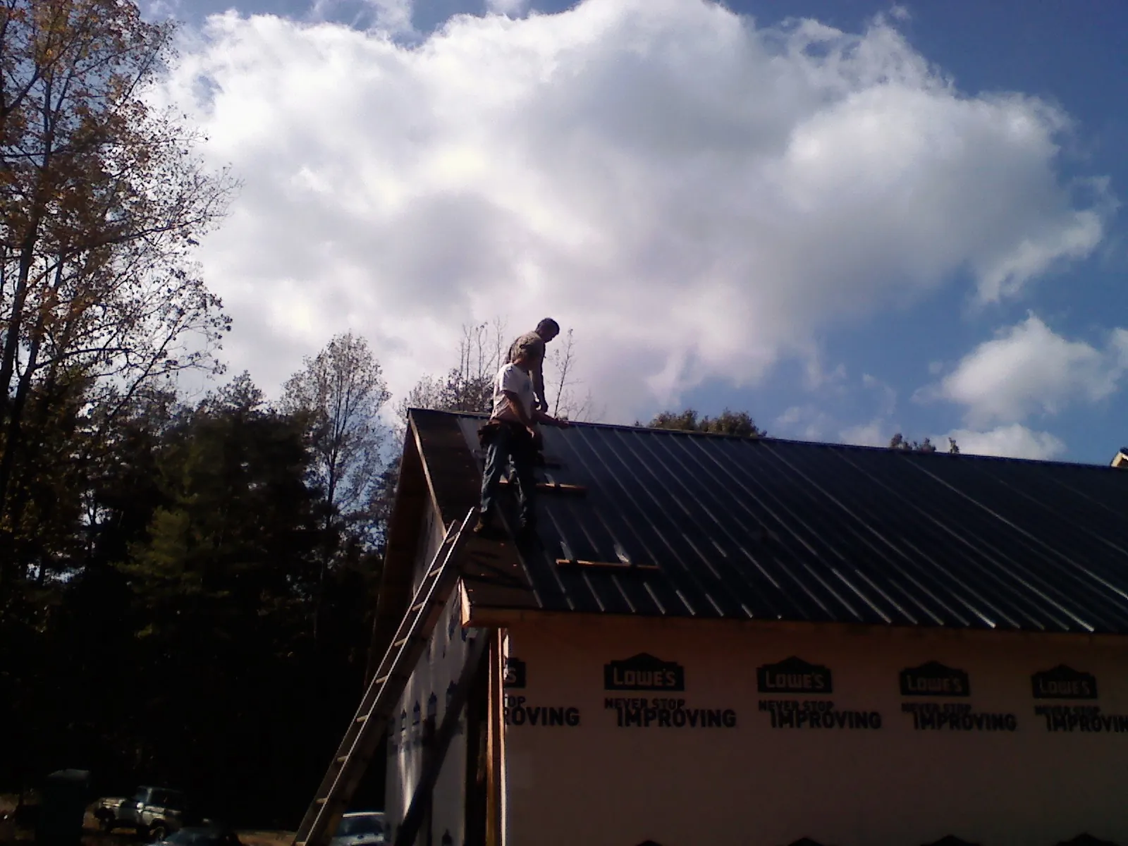 Roofer fastening dark metal panels high against a cloudy sky, from a Roof Inspection job in Bainbridge