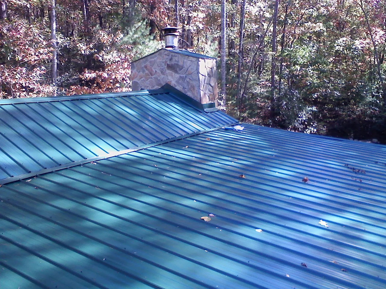 New green metal roof and stone chimney surrounded by autumn woods in Bainbridge